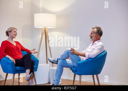 Mature man and young woman sitting in armchairs talking Stock Photo