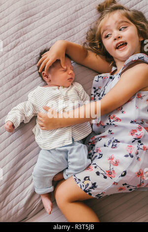 Playful girl lying on blanket cuddling with her baby brother Stock Photo