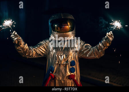 Spaceman standing on a road at night holding sparklers Stock Photo