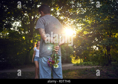 Young man meeting his girlfriend in a park, gifting her with flowers Stock Photo