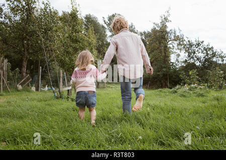 Back view of brother and his little sister walking barfoot on a meadow Stock Photo