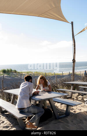 Young couple using digital tablet, sitting a ta a table at the beach Stock Photo