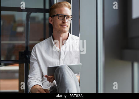 Smiling businessman sitting on windowsill with tablet Stock Photo