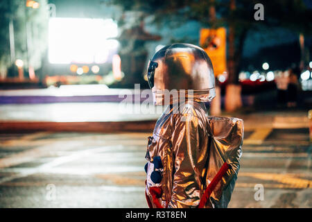 Spaceman on a street in the city at night attracted by shining projection screen Stock Photo