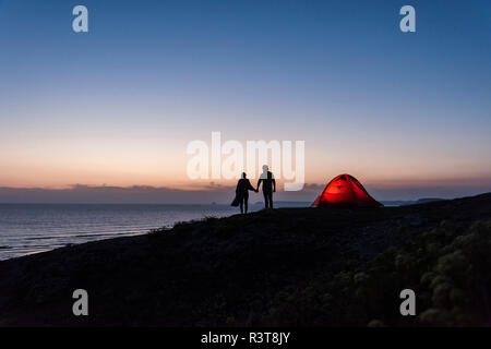 Romantic couple camping on the beach, walking in twilight, holding hands Stock Photo
