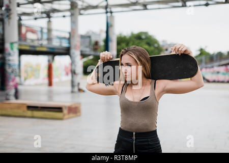 Cool young woman carrying skateboard in the city