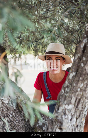 Portrait of smiling woman behind olive tree Stock Photo