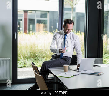 Businessman with atomic model using laptop  in his office Stock Photo