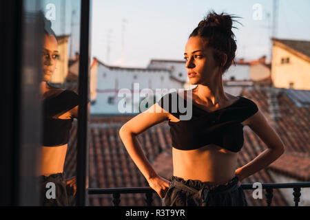 Beautiful young woman standing on balcony at sunset Stock Photo