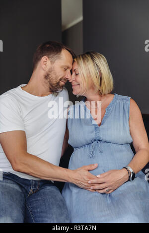 Mature man and his pregnant mature wife sitting on bed touching her belly Stock Photo