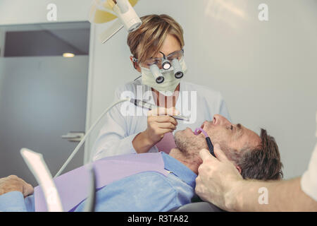 Patient getting dental treatment, dentist using dental drill and head magnifiers and light Stock Photo