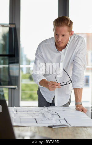 Young man working on blueprint on desk in office Stock Photo