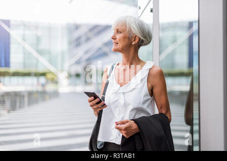 Senior woman with cell phone in the city looking around Stock Photo