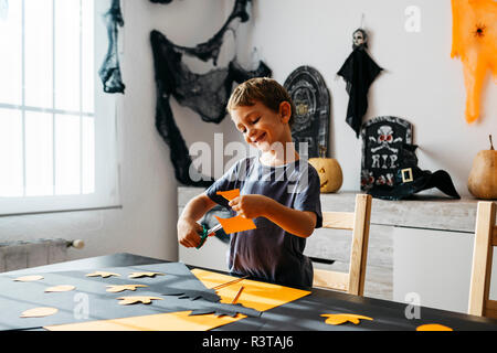 Smiling little boy cutting out for Halloween decoration at home Stock Photo