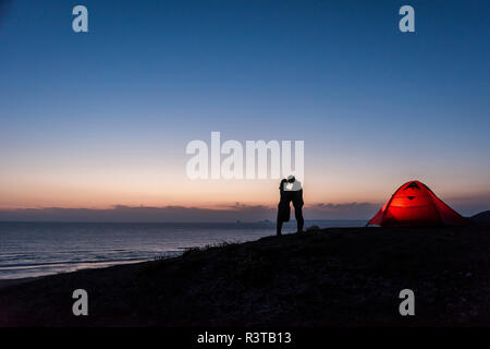 Romantic couple camping on the beach, kissing in twilight Stock Photo