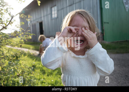 Portrait of screaming little girl covering eyes with her hands Stock Photo