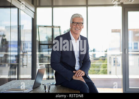 Successful manager sitting on desk, smiling Stock Photo