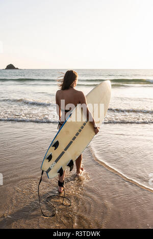 Young woman walking in water, carrying surfboard Stock Photo