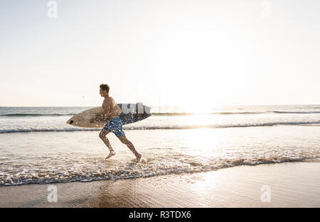 Young man running on beach, carrying surfboard Stock Photo
