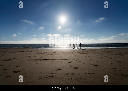 Young couple walking with their dog on the beach Stock Photo