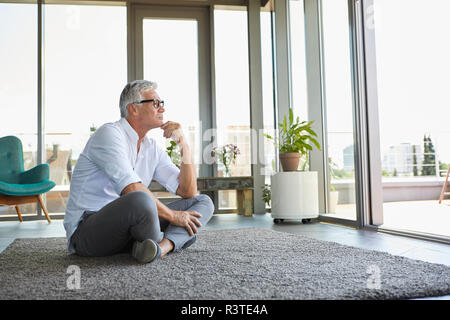 Pensive mature man sitting on carpet at home Stock Photo
