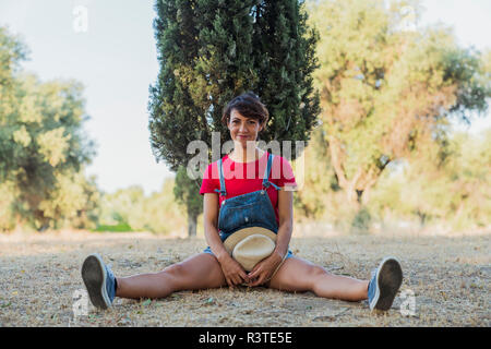 Portrait of smiling woman sitting on the ground in nature Stock Photo