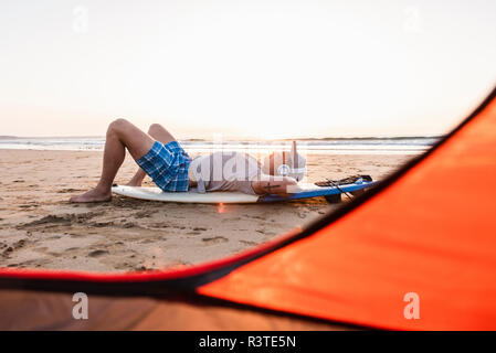 Young surfer relaxing on the beach, listening music Stock Photo