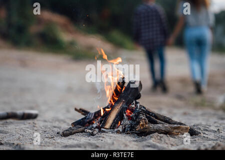 Burning campfire at the riverside, couple in background Stock Photo