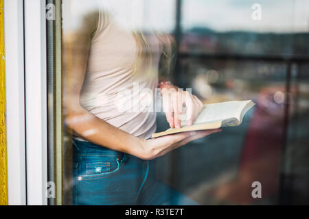 Close-up of young woman reading a book behind windowpane Stock Photo