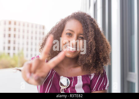 Portrait of smiling young woman showing victory sign Stock Photo