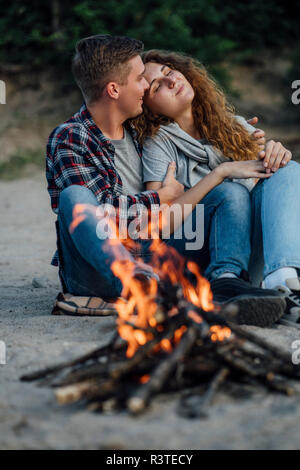 Romantic couple sitting at a campfire at he riverside Stock Photo