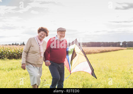Happy senior couple walking with kite in rural landscape Stock Photo