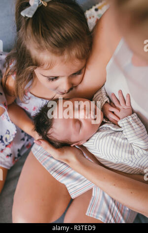 Mother holding her baby close with sister looking at him