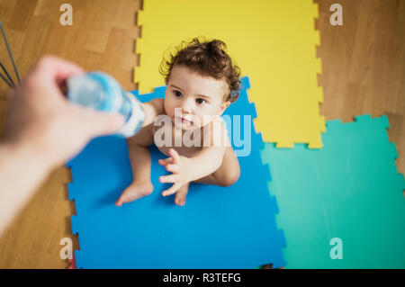 Father's hand giving baby boy a bottle of water Stock Photo