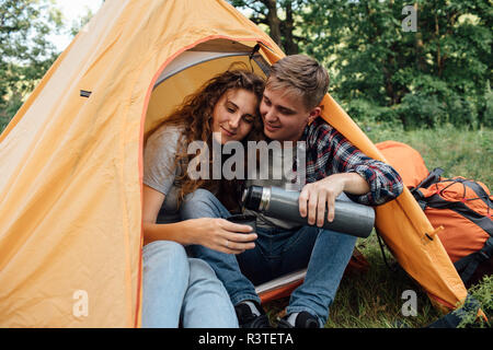 Young couple sitting in tent, drinking tea