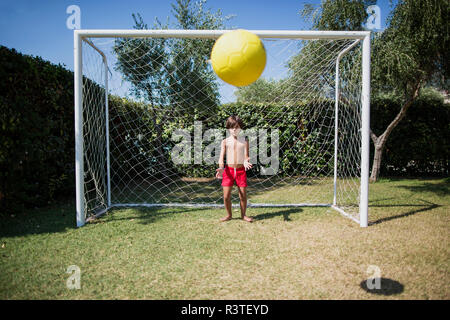 Little boy standing in front of soccer goal watching football Stock Photo