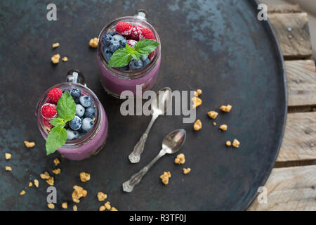 Two glasses of yoghurt with peanut granola, aronia powder and topping of chopped hazelnuts and frozen berries Stock Photo