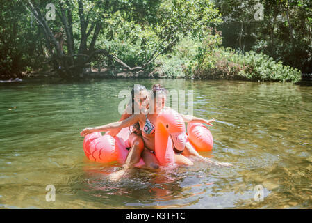 Two friends splashing in water on a floating flamingo Stock Photo