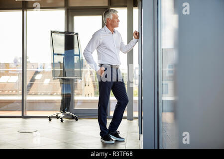 Worried businessman standing in office, looking out of window Stock Photo