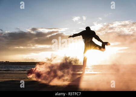 Man doing movement training at the beach with colorful smoke at sunset Stock Photo