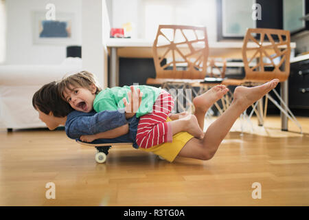 Two brothers at home lying on skateboard together having fun Stock Photo