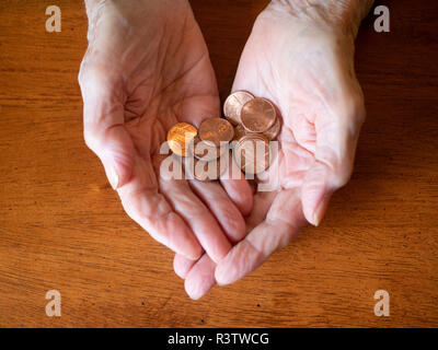 Close up of elderly woman's hands holding pennies. Photographed from above with a wooden table in the background. Stock Photo