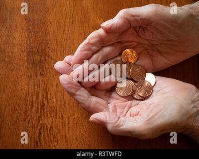 Close up of elderly woman's hands holding pennies. Photographed from above with a wooden table in the background and copy space. Stock Photo
