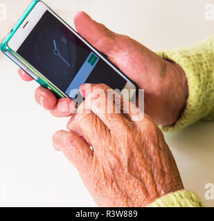 Old woman holding smartphone in her hands. Elderly woman looking at a smart phone inside her home Stock Photo