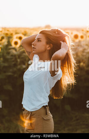 Portrait of a young woman standing in a field of sunflowers, hands in hair Stock Photo
