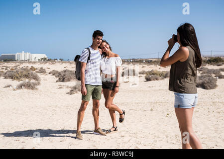 Young woman taking pictures of a young couple on the beach Stock Photo