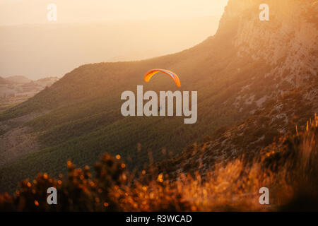 Spain, Silhouette of paraglider soaring high above the mountains at sunset Stock Photo