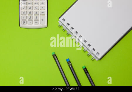 Calculator, notepad and black pencils on a green background. Stock Photo