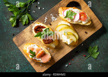 Italian Antipasti snacks set for Wine. Variety Brushetta with Soft Cheese, Pear, Radish, Salmon and Dried Tomatoes served on a rustic wooden board on  Stock Photo