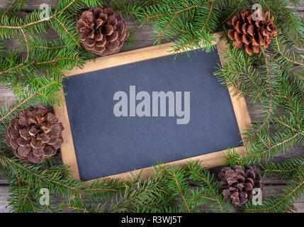 Blank chalkboard bordered with pine cones and evergreen tree branches on a wooden surface Stock Photo